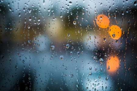 Rain drops on window. Peaceful evening or night at home when raining outside. Water drops on glass. Surface of wet glass. Water splash. City lights bokeh during the rain.の写真素材