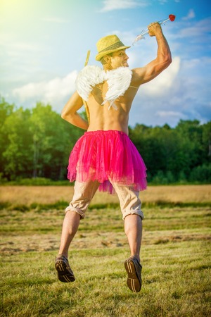 White guy with wings on his back. He displays bow with arrow. Cupid on Valentine's day with pink dressの写真素材