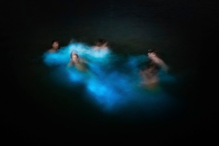 Blurred group of people swimming in glowing waters bio bayの写真素材