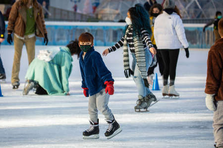 NY, NY, USA - Jan. 22, 2021: Kids learning to skate wearing protective masks on ice rink with...