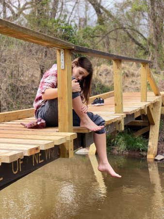 Young attractive girl resting feet after a long hike on the bridgeの写真素材