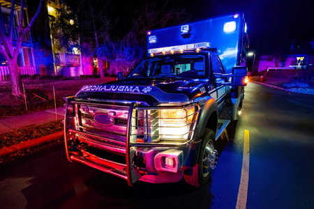 Close up emergency ambulance truck illuminated at night driving through streetの写真素材