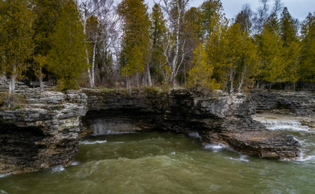 View from the water showing the rugged limestone cliffs and rocky shoreline of Cave Point County Park in Wisconsin with waves and forest backdrop.の写真素材
