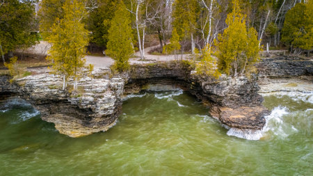 View from the water showing the rugged limestone cliffs and rocky shoreline of Cave Point County Park in Wisconsin with waves and forest backdrop.の写真素材