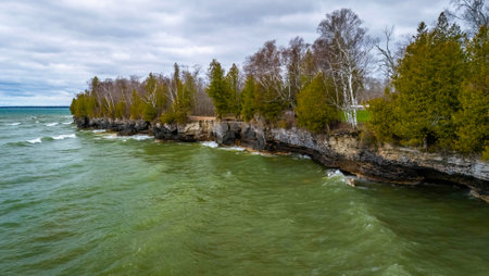 View from the water showing the rugged limestone cliffs and rocky shoreline of Cave Point County Park in Wisconsin with waves and forest backdrop.の写真素材