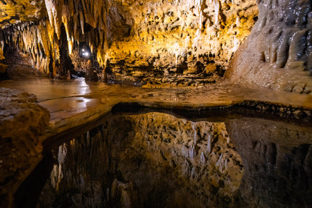 Interior view of Cave of the Mounds in Wisconsin showing illuminated stalactites and stalagmites reflected in still cave water under dramatic lighting.の写真素材