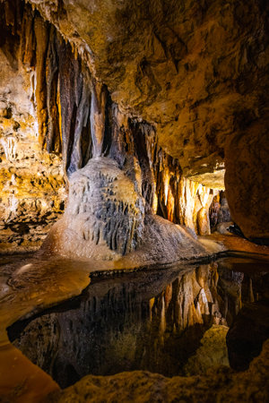 Interior view of Cave of the Mounds in Wisconsin showing illuminated stalactites and stalagmites reflected in still cave water under dramatic lighting.の写真素材
