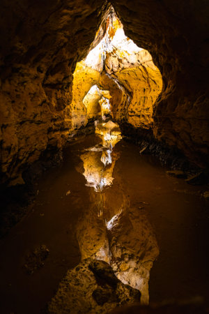 Interior view of Cave of the Mounds in Wisconsin showing illuminated stalactites and stalagmites reflected in still cave water under dramatic lighting.の写真素材