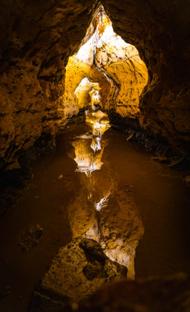 Interior view of Cave of the Mounds in Wisconsin showing illuminated stalactites and stalagmites reflected in still cave water under dramatic lighting.の写真素材