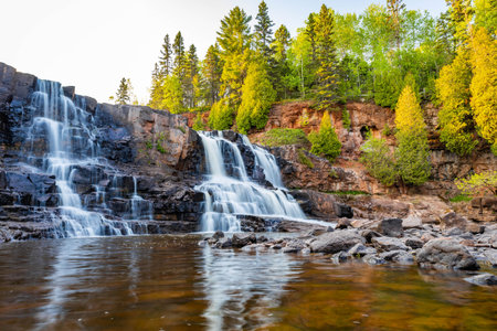 A scenic view of Middle Falls at Gooseberry Falls State Park during a golden sunset, showcasing the beauty of the cascading waterの写真素材