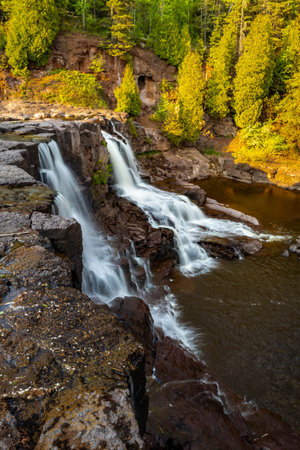 A scenic view of Middle Falls at Gooseberry Falls State Park during a golden sunset, showcasing the beauty of the cascading waterの写真素材