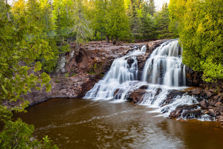 A scenic view of Middle Falls at Gooseberry Falls State Park during a golden sunset, showcasing the beauty of the cascading waterの写真素材