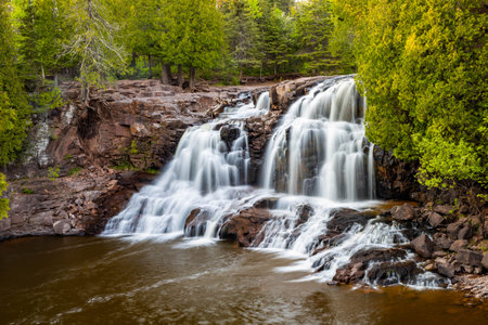 A scenic view of Middle Falls at Gooseberry Falls State Park during a golden sunset, showcasing the beauty of the cascading waterの写真素材