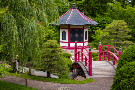 A beautiful traditional red bridge arches gracefully over water in the serene Normandale Japanese Gardenの写真素材