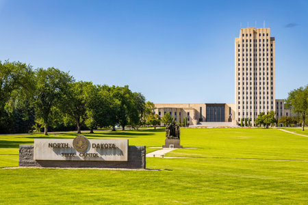 The official North Dakota State Capitol sign prominently displayed on the lush green lawn in front...