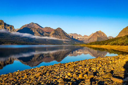 A beautiful sunrise is captured over the tranquil waters of Lake Sherburne, illuminating the...