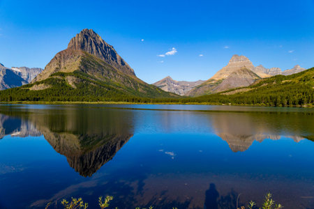 A beautiful sunrise is captured over the tranquil waters of Swiftcurrent Lake, illuminating the...