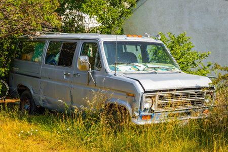 An old, rusty minivan, a symbol of decay and neglect, is captured abandoned in a field of tall, wild grassの写真素材