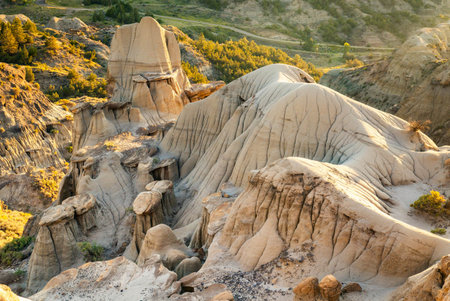 A dramatic sunset casts a golden glow over the unique hills and badlands formations of Makoshika State Parkの写真素材