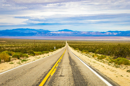 Road crosses Mojave Desert valley and mountain range at sunset in California Nevada Arizona and Utah