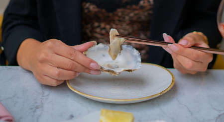 woman eating oysters with chopsticks sitting at the table outside the restaurant. Concept of luxury