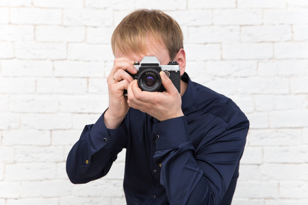 Elegant young man with old rare photo camera on white brick backgroundの写真素材