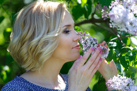 Beautiful young blond woman sniffing lilac bushの写真素材