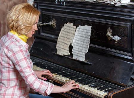 Smiling female musician playing sheet music on retro pianoの写真素材