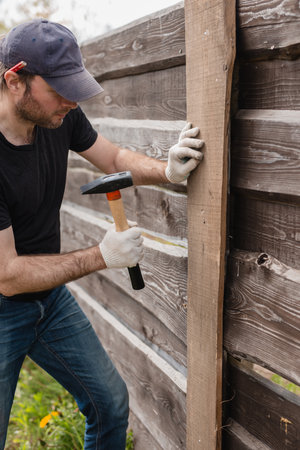 An adult man is engaged in carpentry work at a house construction site - a wooden fence and terrace boardsの写真素材