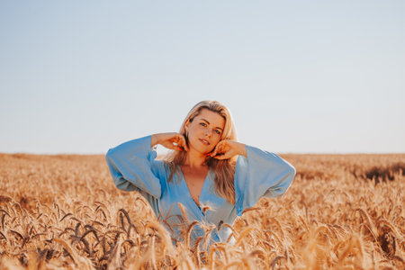 Beautiful adult blonde woman in summer in a field among ears of corn enjoys the warmth and fragrance of flowers - a portrait of a charming beautyの写真素材