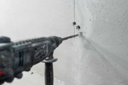 Builder electrician makes a hole puncher in a concrete wall for installation of electrical cables - interior decoration - hidden wiringの写真素材