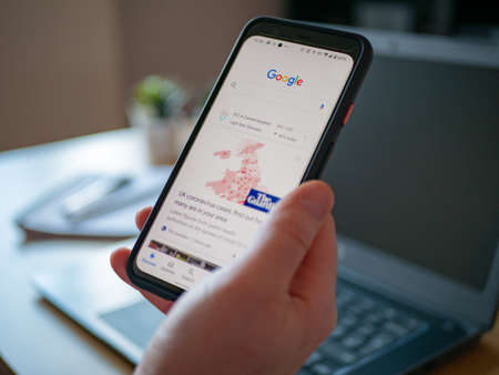 March 2020 UK: Staying at home working on laptop viewing news on phoneのeditorial素材