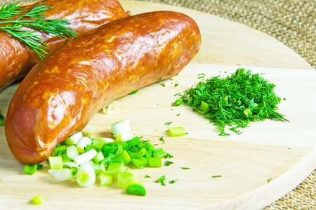 Two smoked sausage and sliced greens lie on a wooden boardの写真素材
