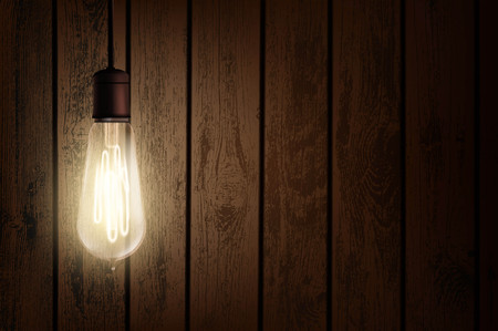 Vintage Edison light bulb is glowing in the dark. Wooden retro background with copy space. Stock vector illustration.のイラスト素材