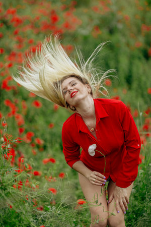 beautiful girl in a field with red poppies in a red shirtの写真素材