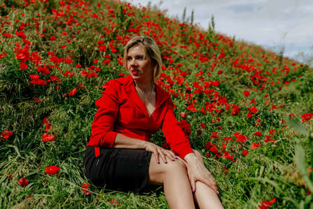 beautiful girl in a field with red poppies in a red shirtの写真素材