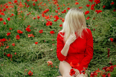 beautiful girl in a field with red poppies in a red shirtの写真素材