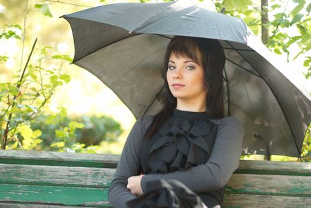Portrait of beautiful girl with umbrella sitting in the parkの写真素材