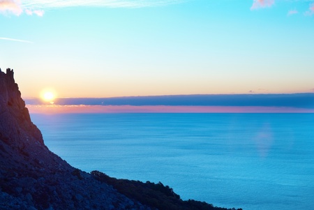 Sunset above the sea with sun, blue sky, clouds and mountainの写真素材