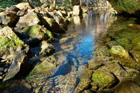 Lake in the forest with rocks and blue sky reflection.の写真素材