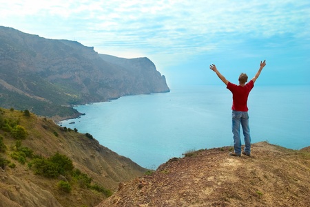 Happy man standing on the cliff with hands up looking at the seaの写真素材