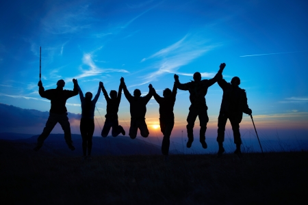 Silhouette of jumping friends in sunset against blue skyの写真素材