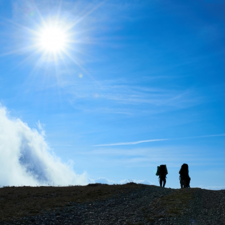 Silhouette of hiking friends against sun and blue skyの写真素材