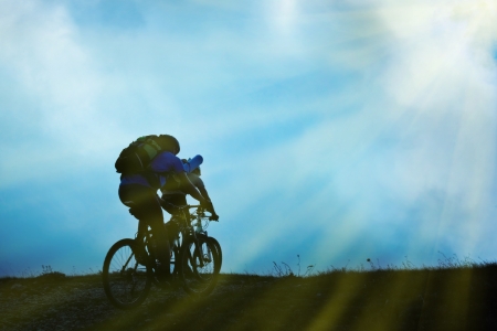 Silhouette of couple on bicycles against clouds and skyの写真素材