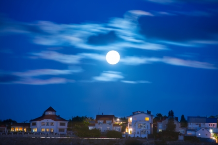 Moon over the river by the town with blue sky and cloudsの写真素材