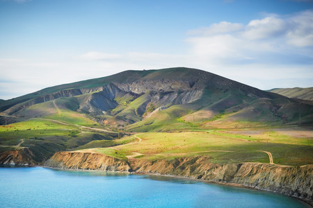 Sea harbor with blue water, green field and blue sky with clouds の写真素材