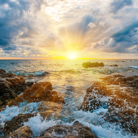 Sunset on the beach with waves, sea, rocks and dramatic skyの写真素材