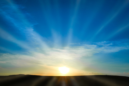 Sun rising above the land on blue sky. Nature background with sunny beamsの写真素材