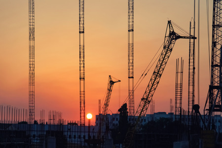 Industrial landscape with silhouettes of cranes on the sunset background