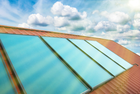 Solar cells on the red house roof under shining sun, blue sky with cloudsの写真素材